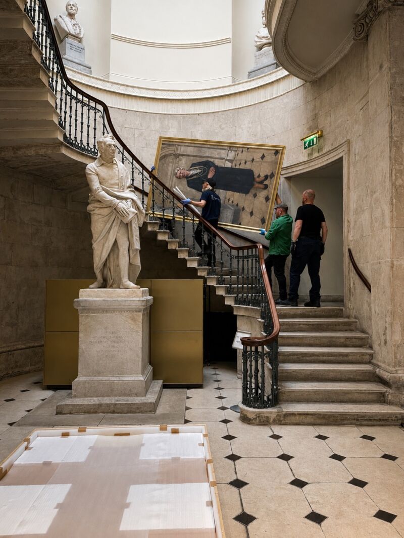 Framed portrait being carried up spiral staircase in museum